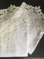 Close-up of the white cotton pillowcases with intricate floral cut-out lace and detailed embroidery.