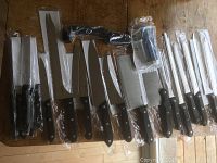Full spread of 18 knives laid out including various types of kitchen knives and accessories, all sealed in plastic.