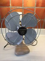 Front view of the vintage Torcan fan showing blades, protective chrome cage and brand emblem in center.