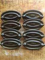 Top view of the set of 8 oval antique brass door pulls arranged in two columns on a wooden surface.