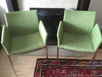 Front view of two green upholstered armchairs with metal frames in front of a fireplace