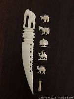Full view of bone letter opener with elephant figure handle and all five tiny carved bone charms featuring camel, horse, peacock, rider on horse, and hand-shaped charm arranged on dark surface.