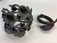 Photo showing both bracelets side by side on a white surface, one black/silver peacock design and one fuchsia serpent design