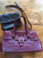 Both handbags placed on wooden surface showing full Coach bag with dual handles and Michael Kors flap bag with chain strap.