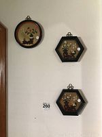 Three oriental themed framed art pieces, two hexagonal and one round, hanging on a white wall, showing their size and style.