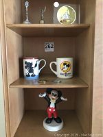 Full display shelf showing all 9 Disney themed collectibles including two coffee mugs, two tokens, two bells, Mickey Mouse figurine, and others.