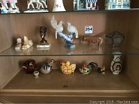 Wide shot of shelf with diverse figurines including alabaster, wood, ceramic, and glass items arranged in two rows