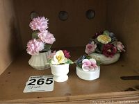 View of four hand painted bone china floral figures on shelf including pink, white and multifloral arrangements.