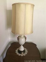 Side view of one lamp showing the full height with shade and the urn base on a wooden table with lace doily.