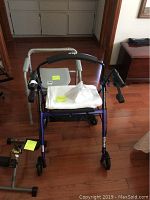Blue walker with four front wheels, padded handles, attached to pedal exercise machine.