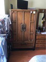 Full view of large wooden armoire with decorative metal handles and bottom drawer