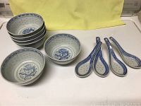 Six 4-inch bowls stacked, two 6-inch bowls and six blue-white ceramic spoons shown on white surface