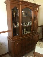 Front angled photo of wooden china cabinet showing glass doors with shelves inside and lower paneled cabinet doors.