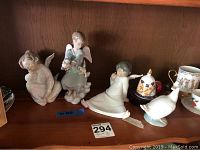 Front view of three Lladro angel figurines and two additional porcelain items on shelf.