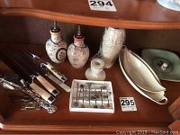 Wooden shelf with six pieces of serving cutlery with cream and black handles, ceramic salt and pepper shakers, ceramic candle holder, small box of pins, and ceramic gravy boat.