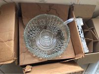 Large glass punch bowl with detailed geometric and floral patterning and glass ladle inside, placed inside a cardboard box.