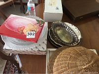 Photo of metal platters with scalloped edges, a rectangular tray, and a wicker basket dome cover on a table with packaged items.