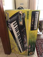 Box showing Yamaha PSR-195 keyboard packaging in yellow with keyboard photo and features.