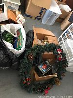 Artificial Christmas wreath decorated with pinecones and red berries inside a cardboard box alongside other holiday decorations.