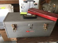 Closed Craftsman metal tool chest with black handle and two rusted latches, with Western Field red box on top.