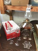 Photo showing oil lamp next to six candlestick holders and small star-shaped glass dish.