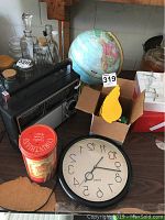 Photo of the world globe, AM/FM radio, wall clock, and coffee container on a table with other glass bottles in the background.