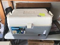 Full view of the Igloo chest cooler placed on a white table indoors showing the latch, handles, and brand label.