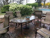 Full view of set on brick patio showing oval table surrounded by six chairs with armrests