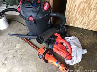 Shop Vac, Black and Decker leaf blower, and hedge trimmer grouped on floor with attachments visible.