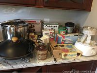 Overview of lot showing various boxed and loose kitchen appliances and cookware on counter, including stock pots, electric wok, and processors.