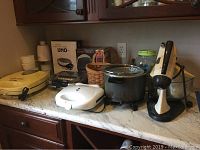 Wide view of all items on counter including waffle makers, grill, deep fryer, mixer, boxed donut maker, basket and more