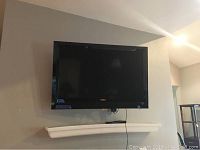 Vizio flatscreen TV mounted on the wall with visible cables and wall bracket below.
