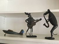 Photo showing two metal musician figurines and a wooden model plane on a white shelf, highlighting the details and size comparison of the items.