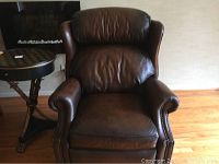 Full front view of dark brown leather recliner chair highlighting cushioned back and armrests with brass trim.