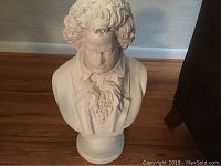 Full view of white ceramic bust on a pedestal, showing the upper torso and base with detailed clothing.