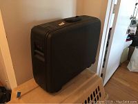 Side view of the black rectangular Delsey hard sided suitcase with handle on top, positioned vertically on a box.