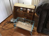 Photo showing both the blue coated wire frame doll bed and the wooden two-stall barn positioned next to each other on a wooden floor.