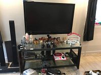 Front view of Vizio flatscreen TV mounted on glass topped media stand with various items on the stand