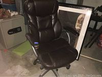Full side/front angled view of brown cushioned office chair showing padded seat, back, and armrests with metal frame and wheeled base on concrete floor.