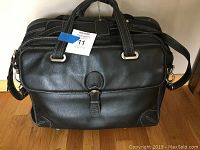 Front view of the Siamod black leather briefcase showing dual handles, front buckle, and attached shoulder strap.