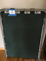 Folding cot folded in half showing metal frame and green fabric surface from above.