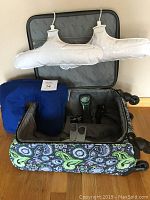 Opened suitcase with inflatable neck pillow, two inflatable hangers hanging inside, Balanzza bag scale and Eddie Bauer mini tripod inside suitcase