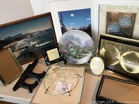 Full group of items on a table including the Thomas Kincade plate, various frames, photos, and display stands