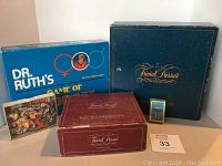 Photo of five boxed vintage games and puzzles together showing Dr. Ruth's Game of Life, two Trivial Pursuit boxes, and card pack