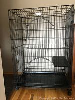 Front view of black foldable metal wire cat cage with one visible perch mounted inside near the middle height.