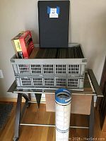 File cart with metal frame, glass top surface, wheels, holding a grey plastic file tote full of letter and legal size hanging folders, black legal size binder on top, and a boxed item to the left (At A Glance calendar).