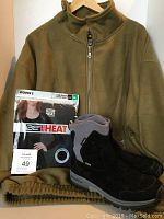 Photo of olive green fleece half-zip pullover hanging on hanger with packaged thermal long sleeve top in front and Merrell boots below