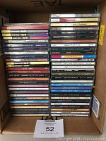 Box filled with music CDs stacked upright showing spines with artist names and album titles