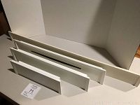 Four stacked wall shelves in white and off-white colors; three smaller shelves and one larger shelf with raised edges