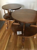 Pair of wooden side tables with round tops and lower shelves, showing overall structure and finish.